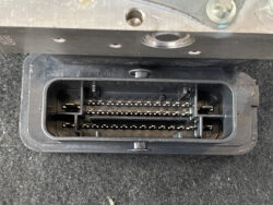 Close-up of a black rectangular automotive connector with two rows of metal pins inside a plastic housing.