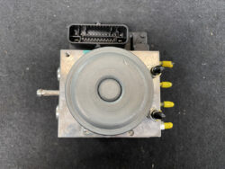 Automotive ABS hydraulic pump module with a round actuator, wiring harness connector on top, and yellow-tipped brake ports on the right side.