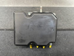 Black rectangular plastic electrical module with yellow terminal pins at the bottom, resting on a dark surface with metal mounting studs on top edges.