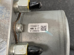 Close-up of a silver motor housing with a white label reading TD8417 AMB Q17 Y120923 and a QR code, with two bolts and a black cap visible.