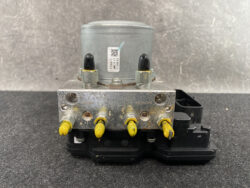 ABS brake module with a metal valve block, yellow-tipped terminals, and a black mounting base.