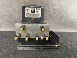 Automotive ABS pump module with six yellow-tipped connectors on a metal block and a black control unit labeled Nissan ABS.
