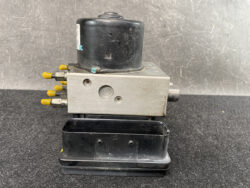 Automotive brake control module with yellow connector pins mounted on a metal block on a black tray (ABS/ESC component).