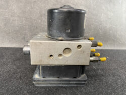Automotive ABS hydraulic control unit: metal valve block with yellow electrical connectors on the side.
