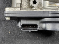 Close-up of a black rectangular automotive electrical connector with several pins on a metal engine component.