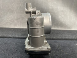 Side view of a gray cast-metal valve or actuator with stacked cylindrical sections and a mounting base, resting on a dark surface.