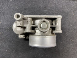 Metal automotive component with a central circular bearing, mounting lugs, and a cylindrical bottom section viewed from above; likely part of a turbocharger or pump system.