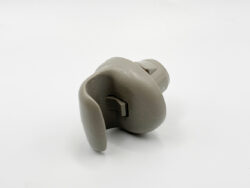 Grey ear mold for a hearing aid resting on a white surface, shown from the side