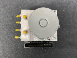 Automotive ABS pump module with yellow-capped ports and a black multi-pin electrical connector, viewed from above.
