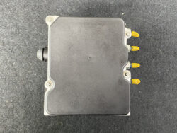 Automotive engine control unit (ECU) with four yellow connector pins on the right and a black sensor/protrusion on the left, on a dark surface.