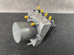 Close-up of a hydraulic control valve block with yellow-tipped actuators and a mounting motor on the side, on a dark surface.
