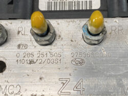 Close-up of a dirty metal engine plate with two yellow-tipped stud nuts labeled RL and RR, along with stamped part numbers and a small Subaru oval logo.