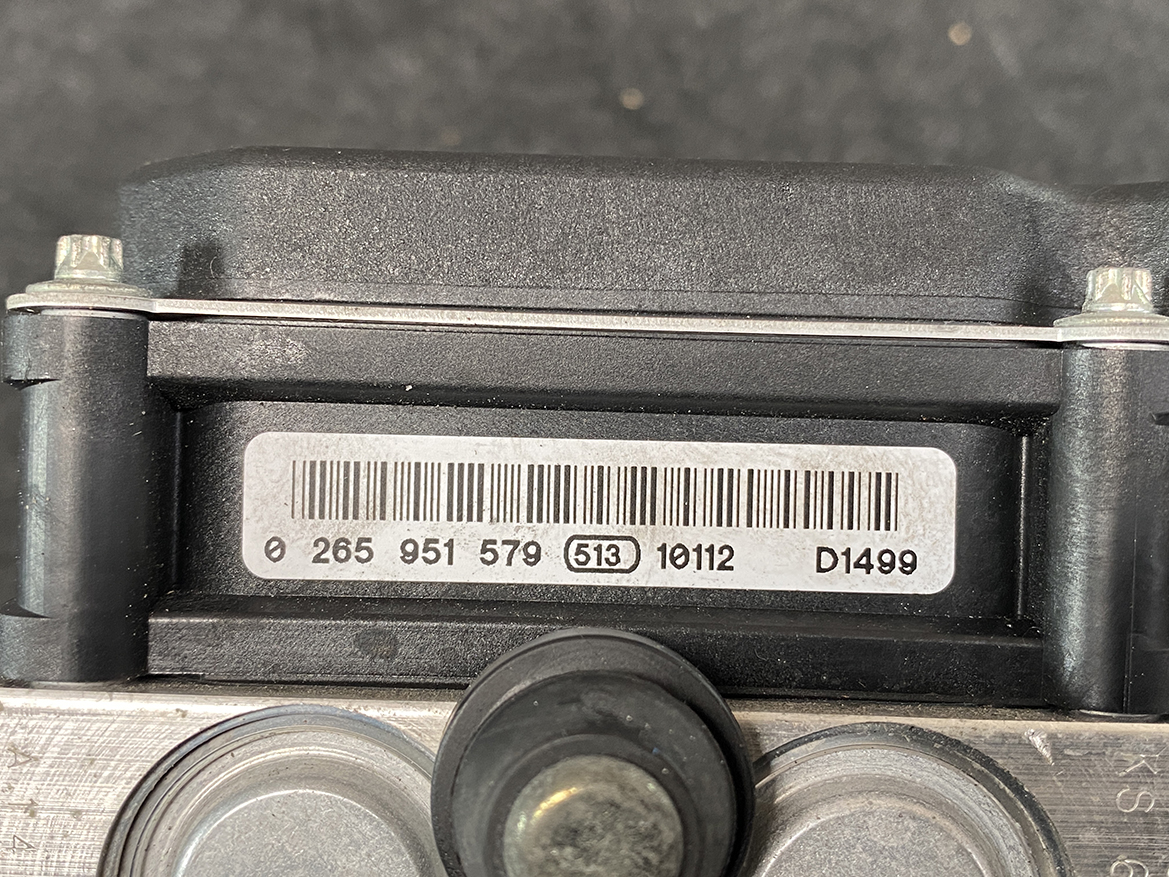 SUB-ACTR-27536SC050_7 Subaru Forester Genuine ABS Pump Module Actuator 27536SC050 » NZ9.95 » JDM-PARTS NZ » JDM-PARTS NZ Close-up of a barcode label with serial numbers on a black plastic industrial housing, flanked by metal bolts and a central knob. Subaru Forester Genuine ABS Pump Module Actuator 27536SC050 » JDM-PARTS NZ