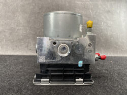 Automotive ABS pump module with a silver hydraulic block, yellow cap, and red electrical terminals on a black base.