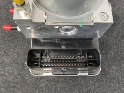 Close-up of a rectangular electrical connector housing with two rows of metal pins inside a dark plastic cavity, mounted to a metal device with red terminal caps visible on the sides.