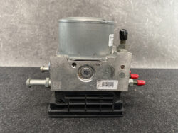 Automotive ABS brake pump modulator with a silver cylindrical motor on top, metal body, and a black plastic base; red-tipped hydraulic ports on the right side.