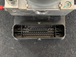 Close-up of a rectangular multi-pin automotive connector with two rows of metal pins in a black housing, mounted under a metal component.