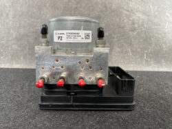 Automotive ABS pump module: gray circular motor on top, metal block with four red terminal posts, mounted on a black base.