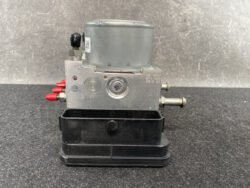 Metal automotive brake modulator with a gray motor on top and red electrical connectors, mounted on a black base.