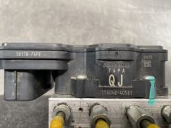 Close-up of a black ADVICS module with the text 'ADVICS 74PA QJ' and serial numbers, mounted on a metal bracket with yellow wire connectors visible nearby.