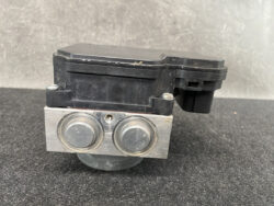 Automotive brake control module (ABS unit) with a black plastic top and a brushed aluminum face featuring two round metal caps.