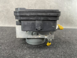 Automotive brake modulator unit with black plastic housing, metal bracket, and yellow electrical connectors attached.