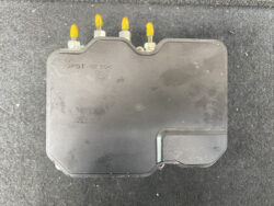 Black automotive electronic control module with four yellow-tipped connectors on top on a dark surface.