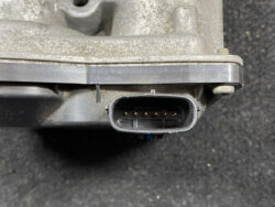 Eight-pin automotive electrical connector on a dusty metal housing, showing gold pins inside the black oval port.