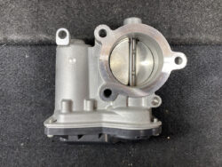 Automotive throttle body with butterfly valve inside a circular intake bore on a silver housing, placed on a dark background, ready for installation or inspection.