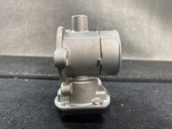 Metallic automotive component with a cylindrical top and mounting flange on a black surface (close-up).