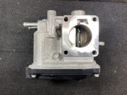 Automotive throttle body with butterfly valve visible inside a circular bore and mounting flange.