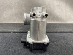 Automotive valve/solenoid component with two hose ports and a black electrical connector on a dark surface.