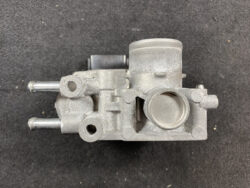 Metal automotive engine component seen from above, featuring a large circular intake bore, two side studs, and multiple mounting features.