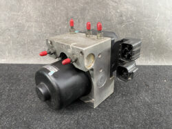 Automotive ABS pump and valve block with electrical connectors and red-tipped ports.