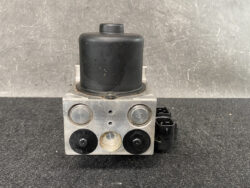 Automotive ABS brake pump module with metal block, black top, and electrical connector on the side.