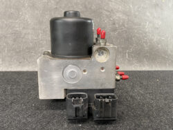 Automotive ABS brake pump module with a black cylindrical top, metal housing, red electrical terminals, and two large plug connectors at the base.