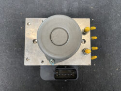 Top view of an automotive ABS brake module with yellow protective caps on side connectors and a multi-pin electrical connector below.