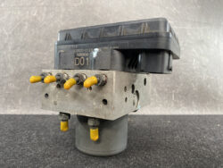 Automotive ABS hydraulic control module with yellow protective caps on ports and a dark control unit on top.