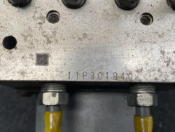 Close-up of a weathered metal plate with serial number 11P301940, a small QR code, and two yellow-wired connectors bolted to it.