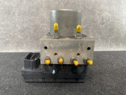 Automotive ABS brake pump module with yellow topped valve screws on a metal block.