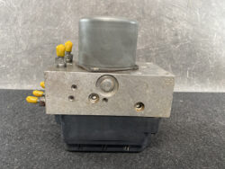 Metal hydraulic control block with yellow port caps and a large gray cap on top, mounted on a black base.