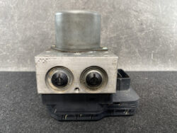 Automotive ABS hydraulic control module with two round ports on a silver metal block and a black plastic base, photographed from the front.