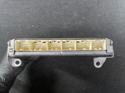 Automotive electronic control unit connector with multiple beige pin sockets and a metal housing held by a gloved hand