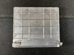 Rectangular metal control module cover with a grid of small square panels on a dark floor.