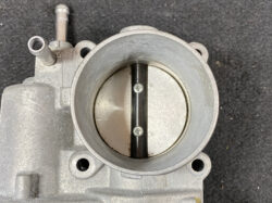 Close-up of a carburetor throttle body with a butterfly valve inside the circular bore.