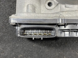 Close-up of a black automotive multi-pin connector with seven gold-plated pins in a row, mounted on a dusty plastic housing.