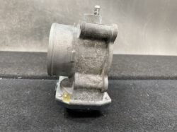 Side view of a dusty, gray automotive turbocharger housing on a mounting base with bolts visible at the base edge.