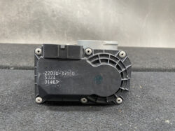 Automotive electronic control module with a circular cooling fan grill on the right and printed part numbers on the front plate.