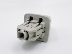 Gray plastic multi-pin electrical connector with a square central receptacle and latch-style tabs, likely a wire-harness plug used in electronics or automotive applications.