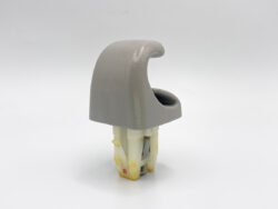 Gray curved plastic cover over a white-yellow mounting clip, likely a fastener component used to join parts.